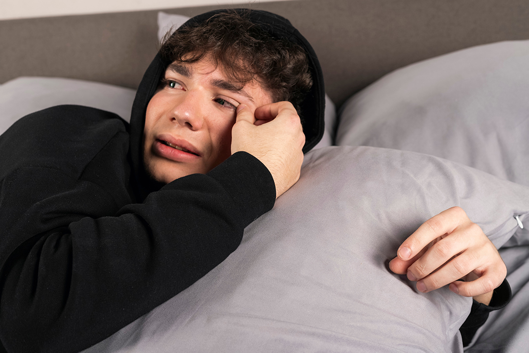 A severely depressed teenager, lies on the bed, embracing a pillow and crying with teary eyes. A young man in a hard mental condition. Sexual abuse concept