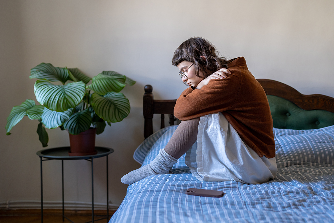 Upset depressed teen girl sitting on bed next to smartphone, feeling lonely and frustrated, sad teenager. Sexual abuse concept