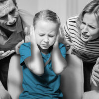 Cries. Poor fair-haired little girl closing her ears and sitting in the armchair while her parents shouting at her